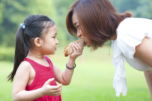 Little Asian girl feeding her mother sandwich outdoor
