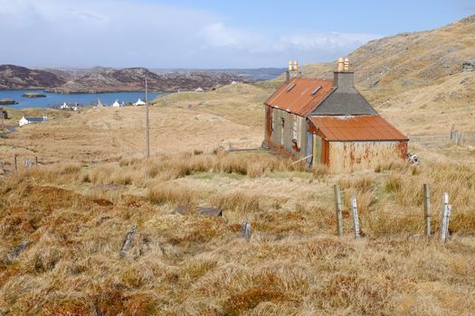 An old derelict building on moorland with tin roof and shed attached and a view to the sea and distant hills.