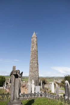 Angel statue before an Ancient round tower and celtic graveyard with cathedral in Ardmore county Waterford, Ireland