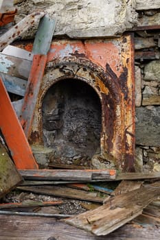 An ornate metal fireplace surround rusty and painted orange amoungst planks and rubble.