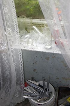 decaying old room window with a windowsill full of dirty glasses and cutlery