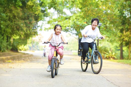 Little Asian girl and grandmother riding on bicycle with great fun