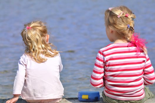 Two blond girls have a picnic on a lakefront