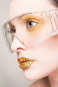 Young caucasian woman with gold fashion makeup wearing clear glasses and gold diamonties on her lips