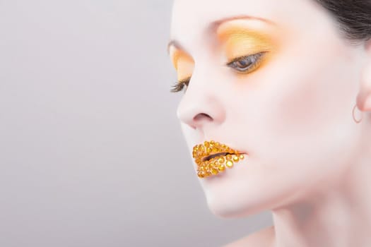 Young caucasian woman with gold fashion makeup and gold diamonties on her lips