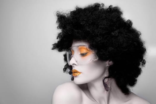 Young caucasian woman with gold fashion makeup and gold diamonties on her lips wearing a black afro wig