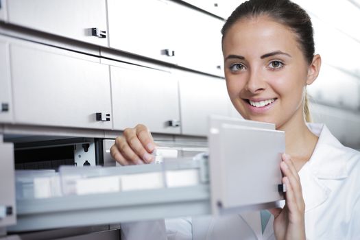 Beautiful young woman pharmacist reaching for medicine