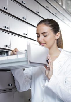 Young woman pharmacist taking medicine from drawer