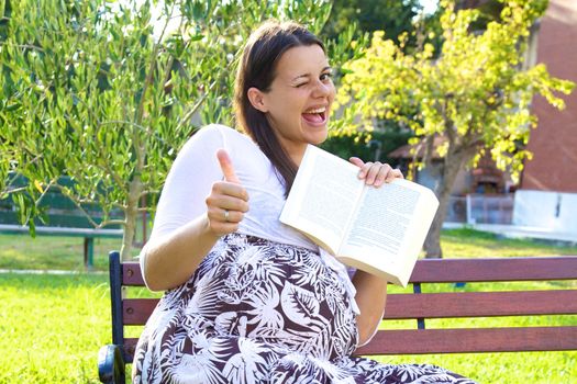 Happy female model pregnant showing book and thumb up