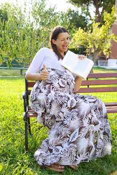 Beautiful pregnant young woman thumb up with book in hand