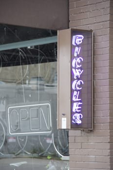 Purple neon bicycle sign on brown brick wall, in front of downtown shop