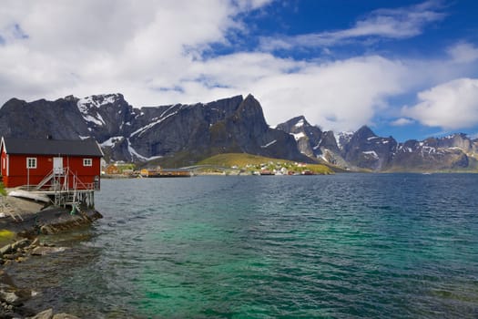 Typical norwegian fjord with fishing hut and high mountains peaks towering above the sea