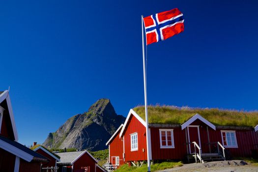 Norwegian flag with typical norwegian red wooden house with sod roof on Lofoten islands