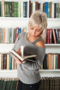blonde holding a book in bookshelf