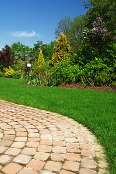 Beautiful spring garden with green lawn, blooming flowers and stone path