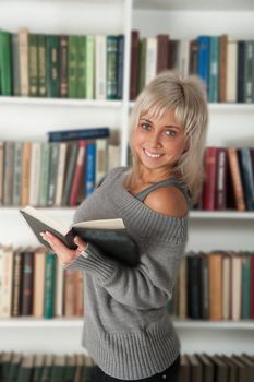 blonde holding a book in bookshelf