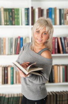 blonde holding a book in bookshelf