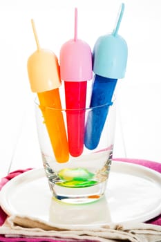 Yellow, red and blue Ice lolly in a glass on white background
