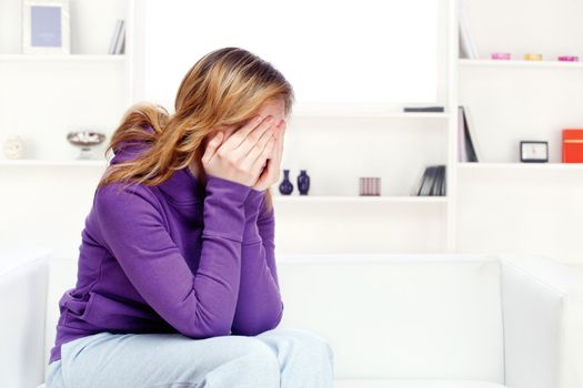 teenager girl at home seating on sofa and covering face with hands