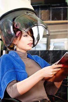 Pretty lady reading a magazine and under bonnet hair dryer