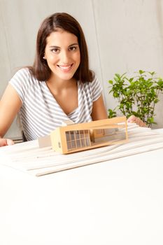 A young female architect smiling at the camera with a house model