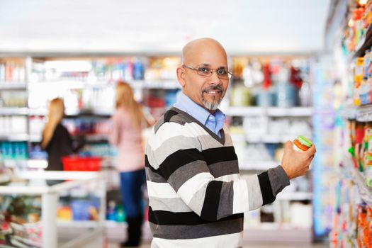 Smiling mature man shopping in the supermarket with people in the background