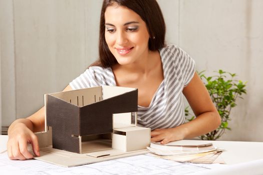 A female architect looking over a model house with blueprints and color swatches on the table