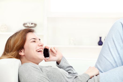 Pretty young woman laying on sofa at home and talking over mobile phone