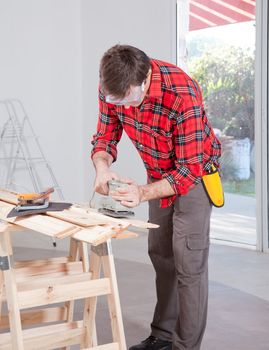 A man at home using an electric hand sander with safety goggles