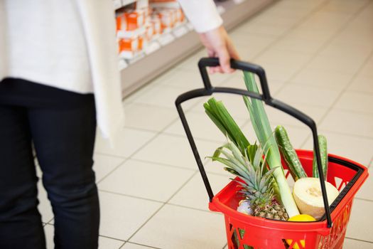 High angle view of human hand carrying red basket filled with fruits and vegetables