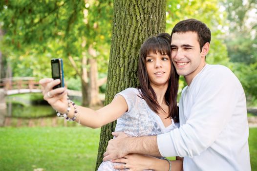young couple in the park, taking picture of themselves with mobile phone