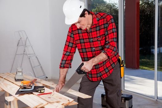 A construction worker using a hand wood saw while wearing a white safety helmet