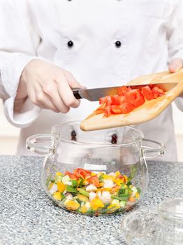 chef adds chopped tomatoes in a glass bowl with other vegetables