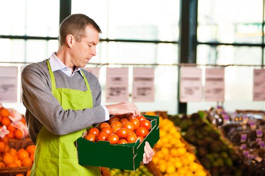 Market assistant wearing apron with holding box of tomatoes in the supermarket