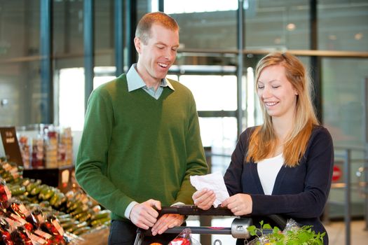 A happy couple with a shopping cart and grocery list in a supermarket