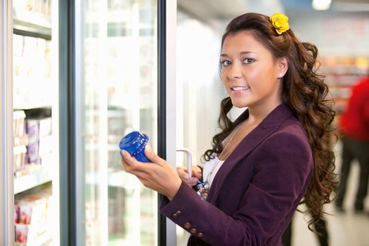 Portrait of a young woman holding container in front of refrigerator in the supermarket