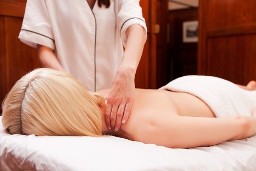 A woman with arms down receiving a shoulder massage in a retro styled spa