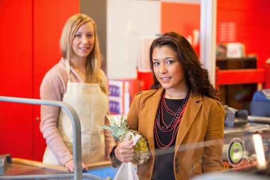 Portrait of a customer holding pineapple with shop assistant in the background