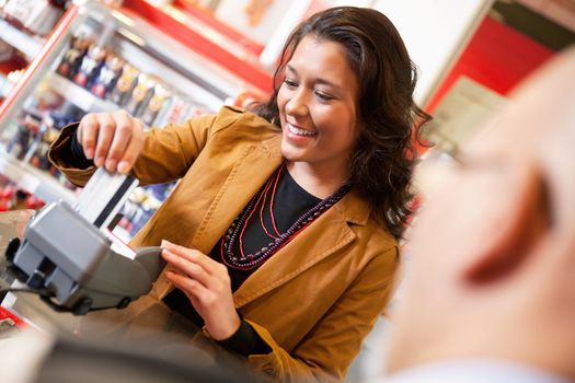 Shop assistant smiling while swiping credit card in supermarket with customer in the foreground