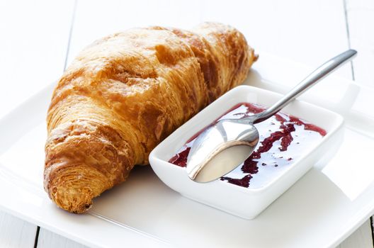 Croissant with raspberry jem on white table