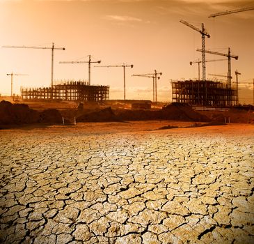 Landscape with construction cranes and cracked soil