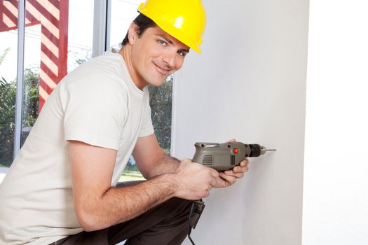 Portrait of smiling man worker with hard hat drilling wall