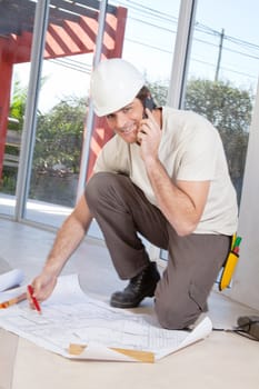 Portrait of a happy construction worker on cellphone with blueprint