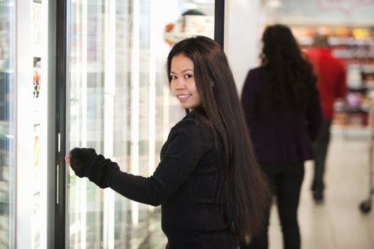 Young woman holding container in front of refrigerator in the supermarket