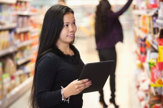 Young woman looking at the products while using digital tablet in shopping centre with person in the background