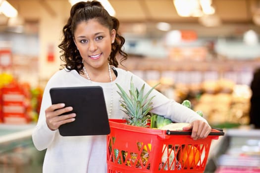 Woman with digital tablet holding fruit basket in shopping centre and looking at camera