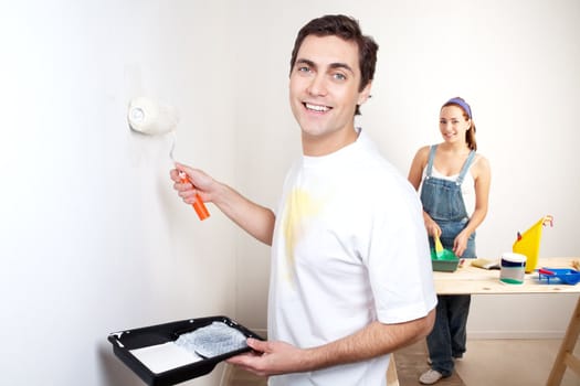 Portrait of smiling man painting the wall with woman standing in the background