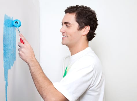 Happy young man applying sky blue color to the wall