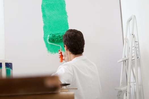Rear view of man painting the wall with a roller of new apartment