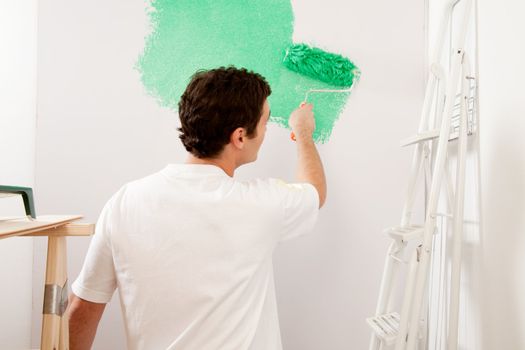 A faceless male painting a wall with a roller brush, home improvements